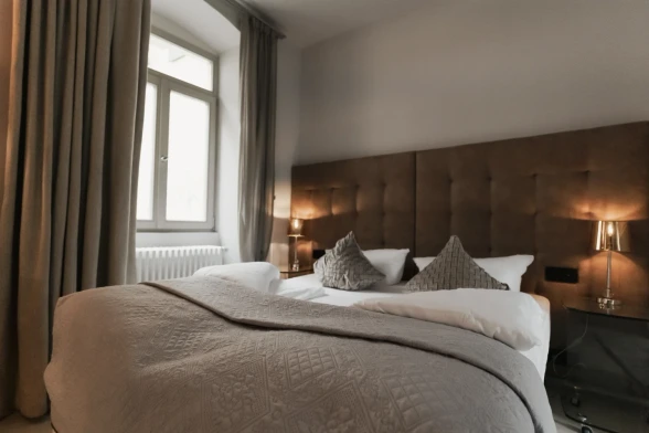 Helles Zimmer mit Fenster, braunen Gardinen und einem Doppelbett mit braunem Kopfbrett. Ferienwohnung 1 von BS Suites Heidelberg